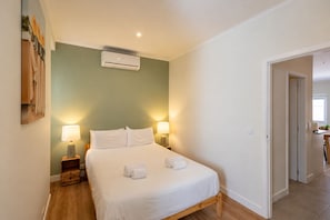 A bedroom with a bed, two bedside lamps, an air conditioning unit, and a door leading to another room. - Stylish Oasis in Trendy Historic Centre Quarter (Lisbon)