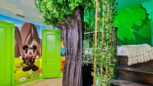 Una stanza con un grande tronco d'albero, porte verdi e un murale di Topolino.