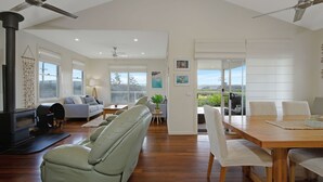 A spacious living area with a fireplace, sofas, a dining table, and a view through a glass door.