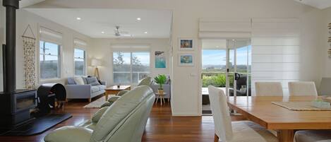 A spacious living area with a fireplace, sofas, a dining table, and a view through a glass door.