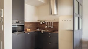 A modern kitchen with dark cabinets, a stainless steel range hood, and a microwave. - Líbere Madrid Malasaña (Madrid)