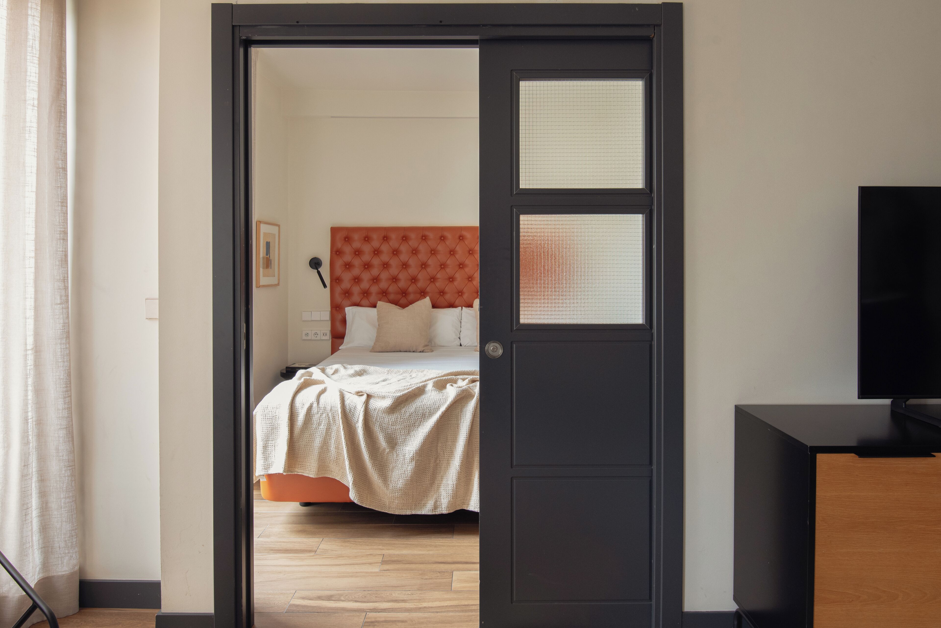A bedroom with a bed, a television, and a wooden floor.