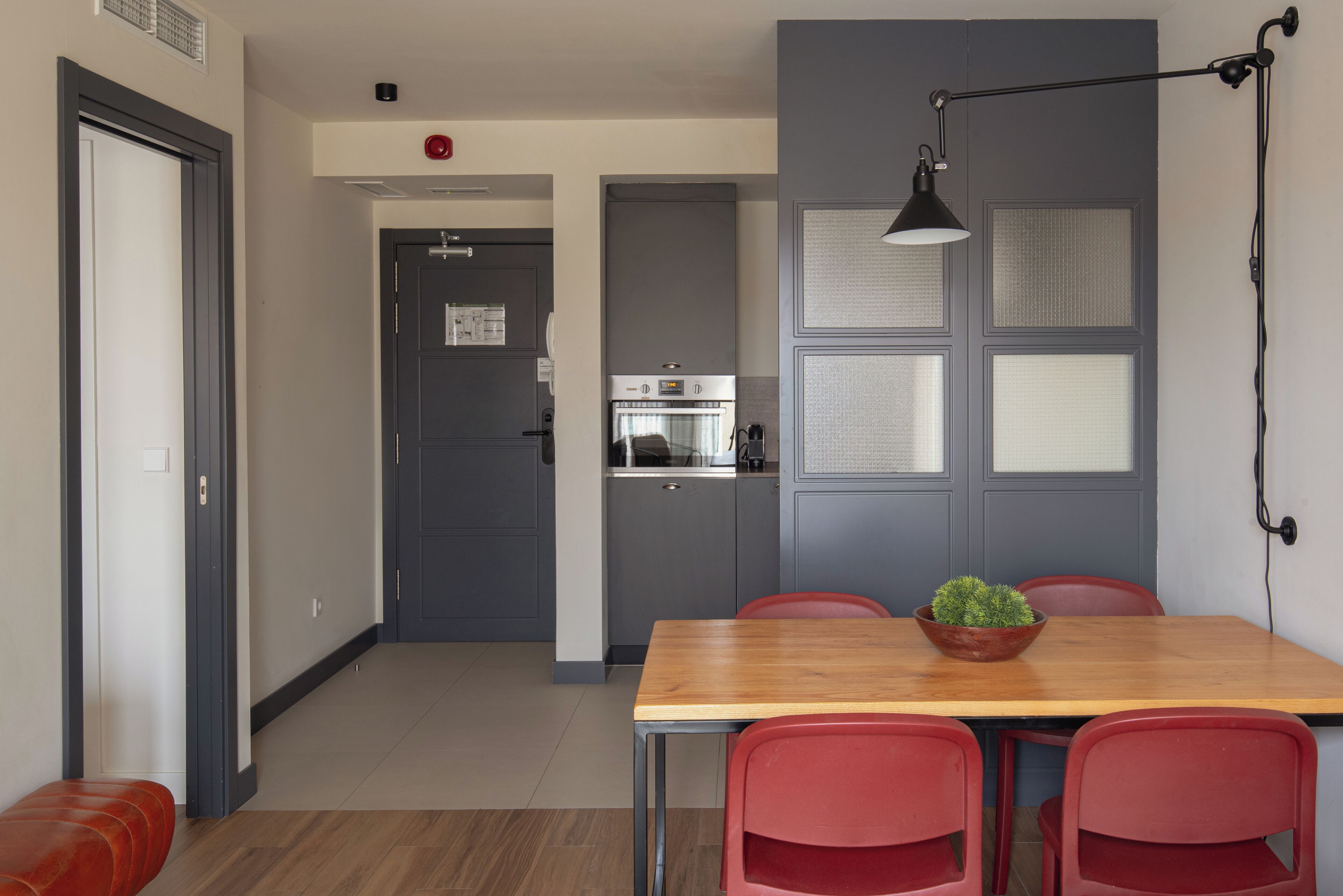 Una cocina compacta con electrodomésticos modernos, una zona de comedor con una mesa de madera y sillas rojas, además de un banco rojo.