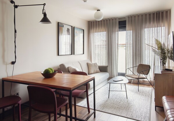 Una sala moderna con una mesa de comedor de madera, sillas rojas, un sofá y una mesa de centro. Hay una planta en maceta sobre la mesa y una ventana grande con cortinas.