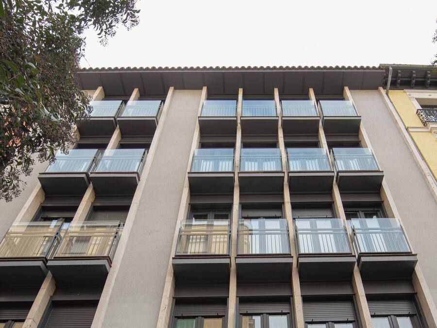 Un edificio de varios pisos con un diseño arquitectónico moderno, con balcones de barandilla de vidrio y una serie de ventanas.