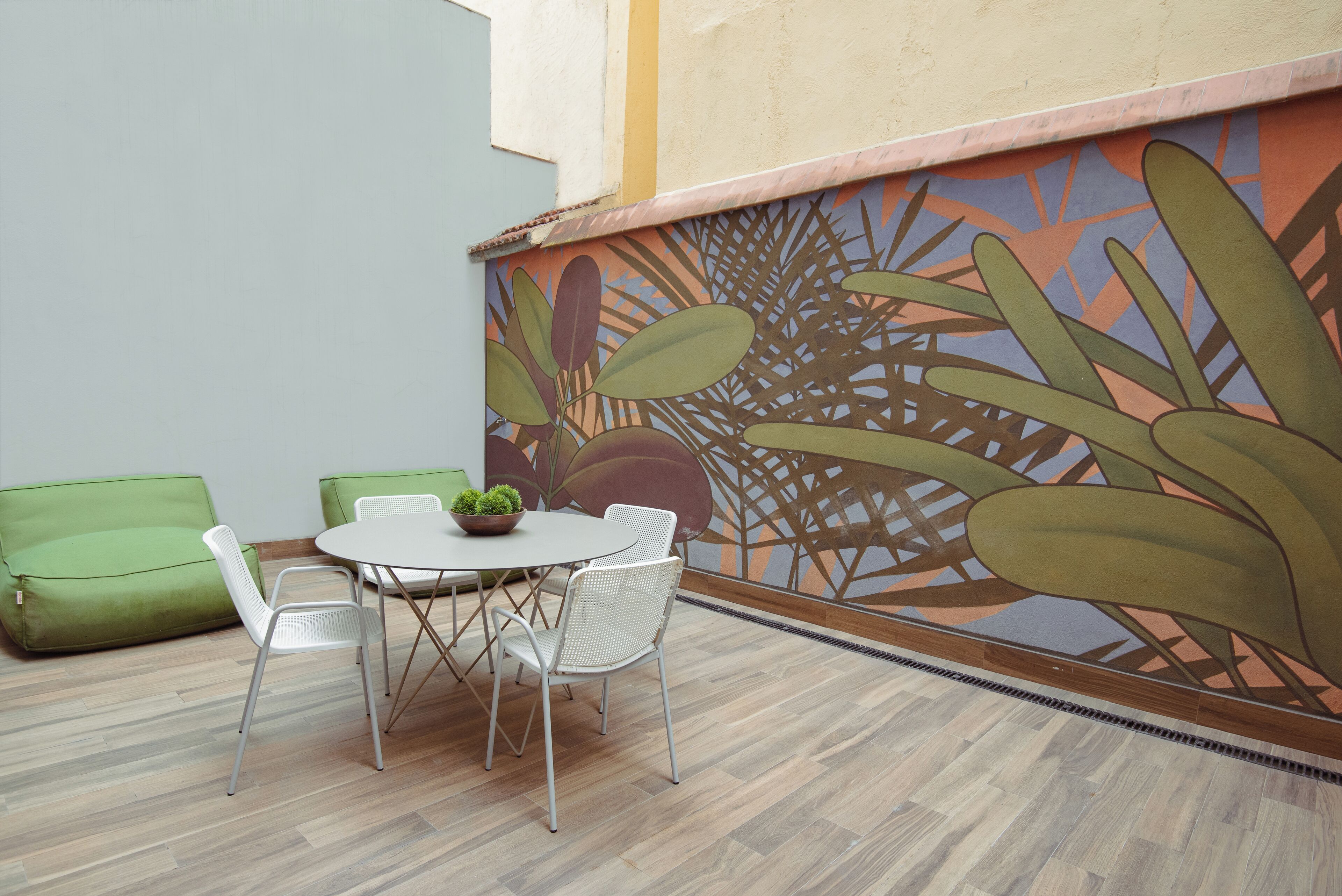 A dining area with a table and chairs, a green sofa, and a mural with plant designs on the wall.