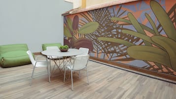 A dining area with a table and chairs, a green sofa, and a mural with plant designs on the wall.