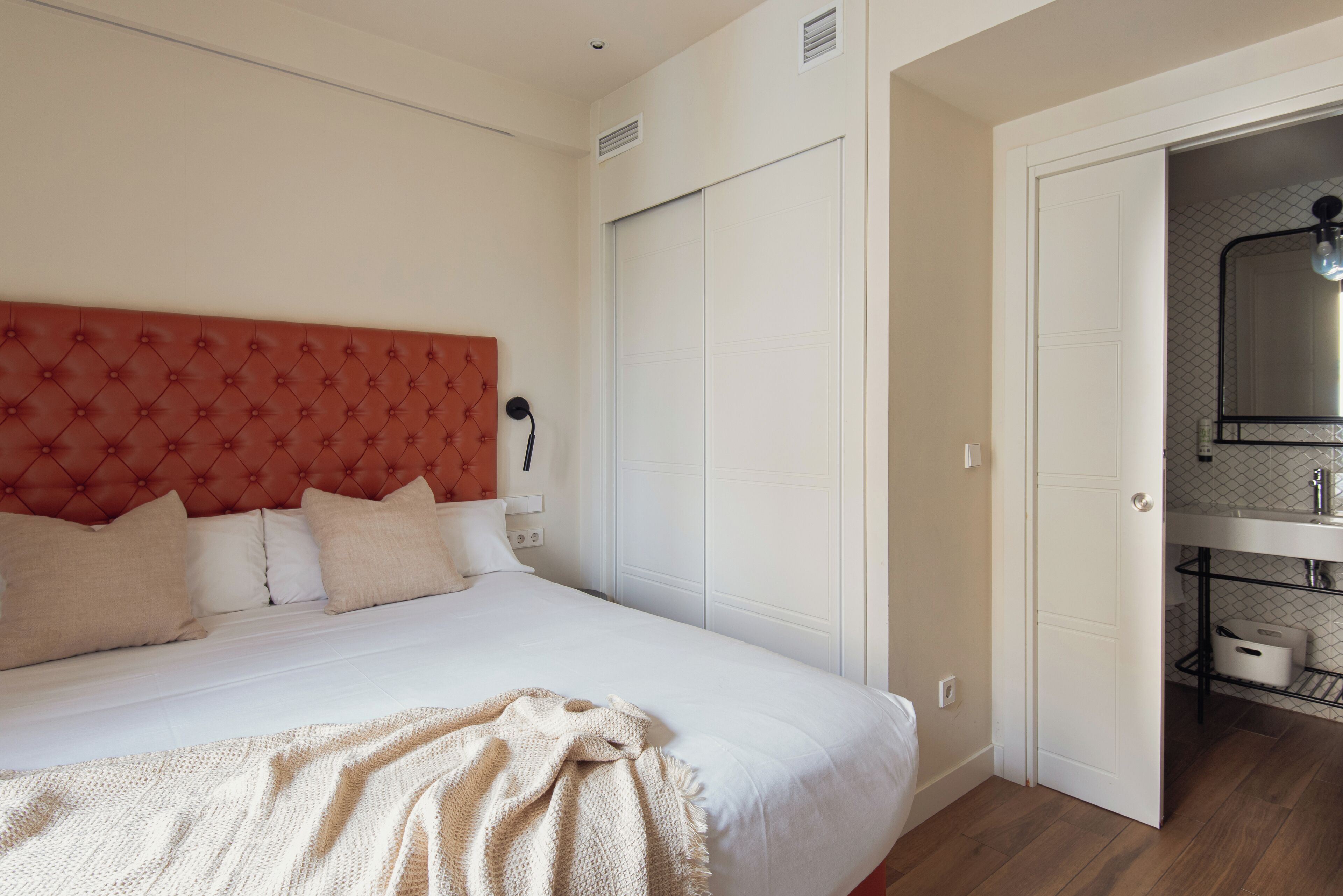 A bedroom with a large bed, a red tufted headboard, white bedding, and a white wardrobe.