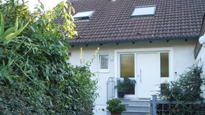 A house with a tiled roof, a white door, and a small garden with a potted plant. - Apartment Noack, 50 m² with Private Terrace, Garden Area, and Wi-Fi (Immenstaad am Bodensee)