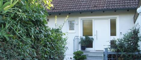 A house with a tiled roof, a white door, and a small garden with a potted plant.