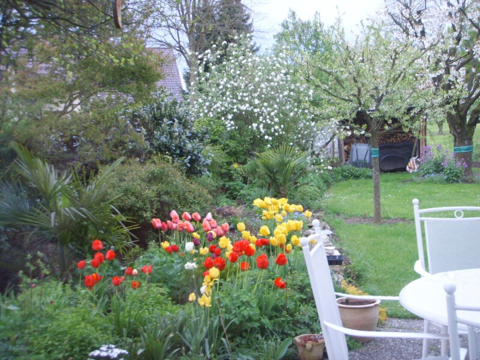 Ein Garten mit verschiedenen Blumen, einem weißen Stuhl und einem Tisch.