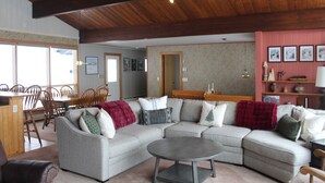 Un salón espacioso con un sofá modular grande, una mesa de centro redonda y un comedor con sillas y mesa de madera.
