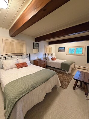 Un dormitorio con dos camas, un banco de madera y una ventana con contraventanas.