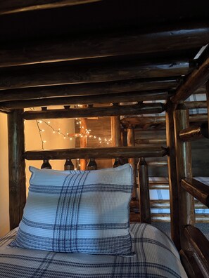 A bed with a plaid pillow and a wooden headboard in a rustic room with string lights.