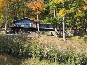 A two-story house with a balcony, surrounded by trees and a stone wall. - Upper Villa at Holiday Valley (Ellicottville)