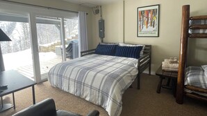 Un dormitorio con cama, una silla, un escritorio, una ventana y un cuadro en la pared.