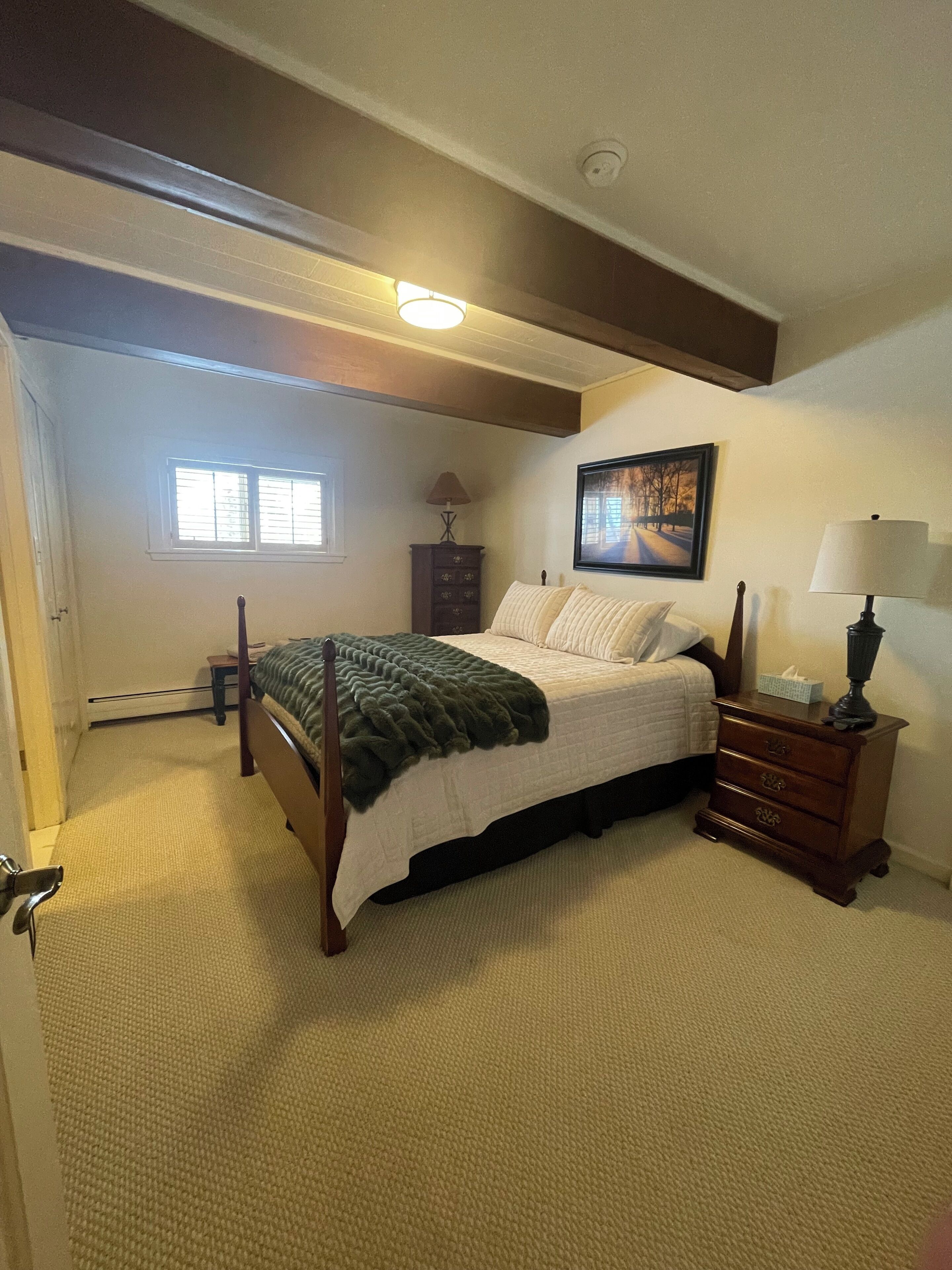 A bedroom with a bed, a dresser, a nightstand, a window, and a painting on the wall.