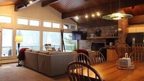 Un salón amplio con un sofá grande, una mesa de comedor de madera y sillas. Hay una chimenea, un televisor y un ventilador de techo.