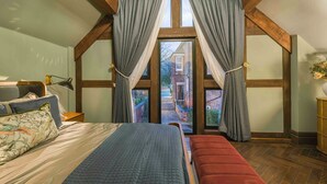 A bedroom with a large bed, a bench, and a view through a window with curtains.