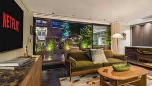 A modern living room with a green sofa, a wooden coffee table, and a large window overlooking a garden.