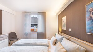 Ein Hotelzimmer mit Bett, Schreibtisch, Stuhl, einem Gemälde an der Wand und Blick durch eine Tür.