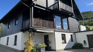 Ein zweigeschossiges Gebäude mit Balkon, großen Fenstern und einer gepflasterten Eingangspforte.