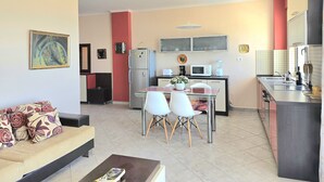 Ein modernes Wohnzimmer mit Sofa, Esstisch und Stühlen, einer Küchenzeile mit Geräte und einer roten Akzentwand.