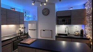 A modern kitchen with built-in appliances, a clock, and a wall-mounted calendar. - Vacation Rental Apartment with Shared Garden, Balcony & Wi-Fi (Bezons)