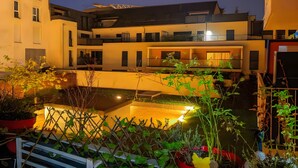 A multi-story building with balconies, a courtyard with water features, and potted plants. - Vacation Rental Apartment with Shared Garden, Balcony & Wi-Fi (Bezons)