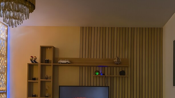 A modern living room with a TV displaying 'NETFLIX,' a wooden entertainment unit, a dark sofa, a small round table with a plant, and a decorative vase. - Vacation Rental Apartment with Shared Garden, Balcony & Wi-Fi (Bezons)