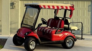 Carro de golf rojo con toldo, estacionado frente a un garaje.