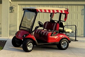 Ein roter Golfwagen mit Verdeck, vor einer Garage geparkt.