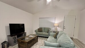 Ein Wohnzimmer mit Fernseher, zwei Sofas, einem Couchtisch und einem Deckenventilator.