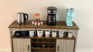 Una estación de café de madera con cafetera, hervidor y un soporte para tazas.