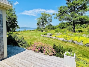 A wooden deck with a view of a landscaped garden and a body of water.
