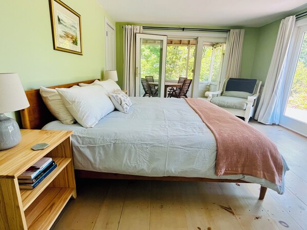 A bedroom with a bed, bedside table, lamp, and a view of the outdoors.