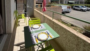 A balcony with a table set for two, chairs, an air conditioning unit, and a view of a parking lot and buildings. - Studio 2OO M Centre Saint Florent -in quiet building. (Saint-Florent)