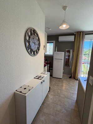 A kitchen with a clock, a white cabinet, a refrigerator, and a window with curtains.