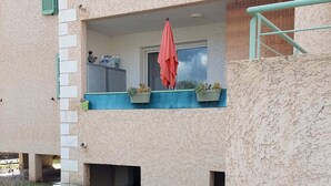 A two-story building with a balcony on the upper floor, featuring a table with potted plants and a red umbrella. - Studio 2OO M Centre Saint Florent -in quiet building. (Saint-Florent)