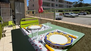 En balkon med et bord dækket til to, en grøn stol, en rød parasol og en bygning i baggrunden.