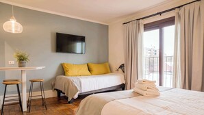 A bedroom with a bed, a desk, two stools, a potted plant, a TV, and a window with curtains. - Trendy Design Studio Vaisse | Modern Santiago Stay (Providencia)
