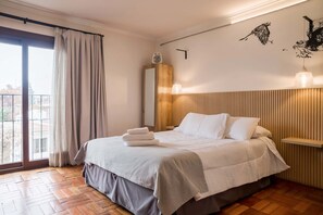 Une chambre à coucher comprenant un lit, une table de chevet, une commode, une fenêtre avec des rideaux et un luminaire fixé au mur.