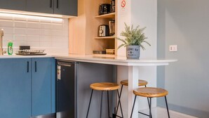 A modern kitchen with blue cabinets, a white countertop, a stainless steel refrigerator, and a hanging pendant light. - Trendy Design Studio Vaisse | Modern Santiago Stay (Providencia)