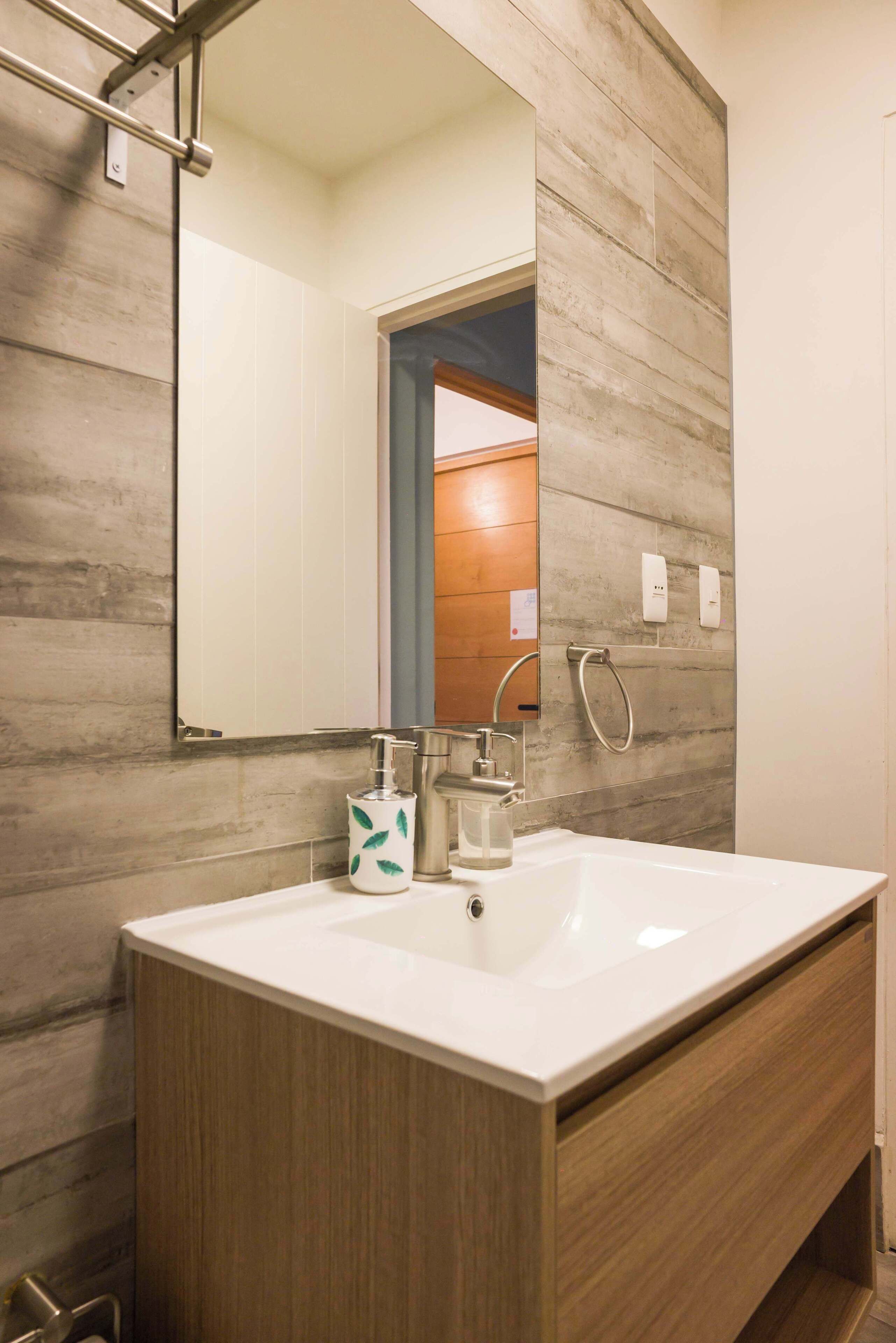 Une salle de bain avec un meuble-lavabo en bois, un lavabo blanc, un miroir et un porte-serviettes.