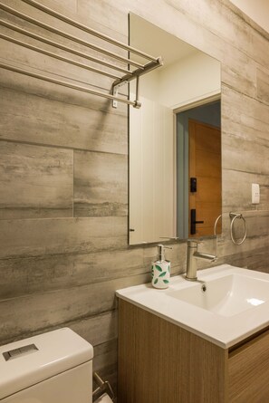 Un baño con lavamanos blanco, espejo, toallero y retrete.