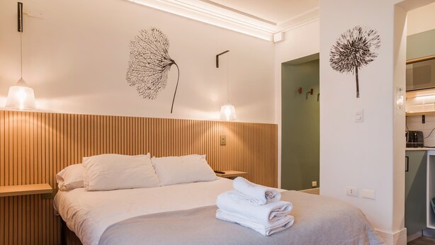 A neatly made bed with white linens and towels, a wooden slat headboard, and wall art depicting dandelions. - Bright & Modern Studio Prime Providencia Location (Providencia)