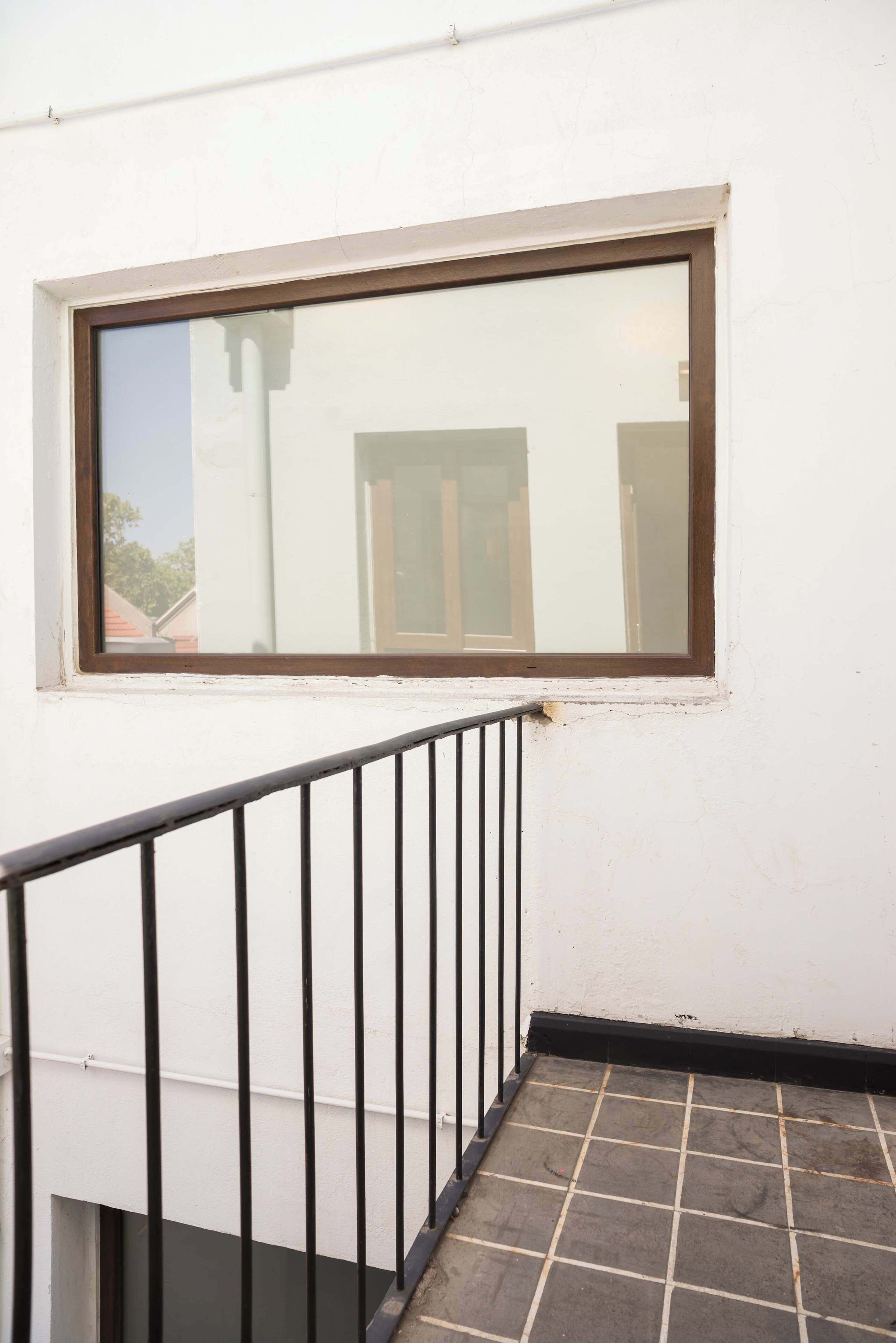 A window with a brown frame, a white wall, and a black metal railing.