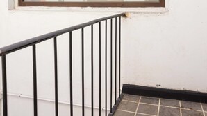 Une fenêtre avec un cadre marron, un mur blanc et une rambarde en métal noir.