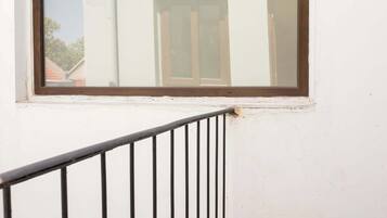 A window with a brown frame, a white wall, and a black metal railing.