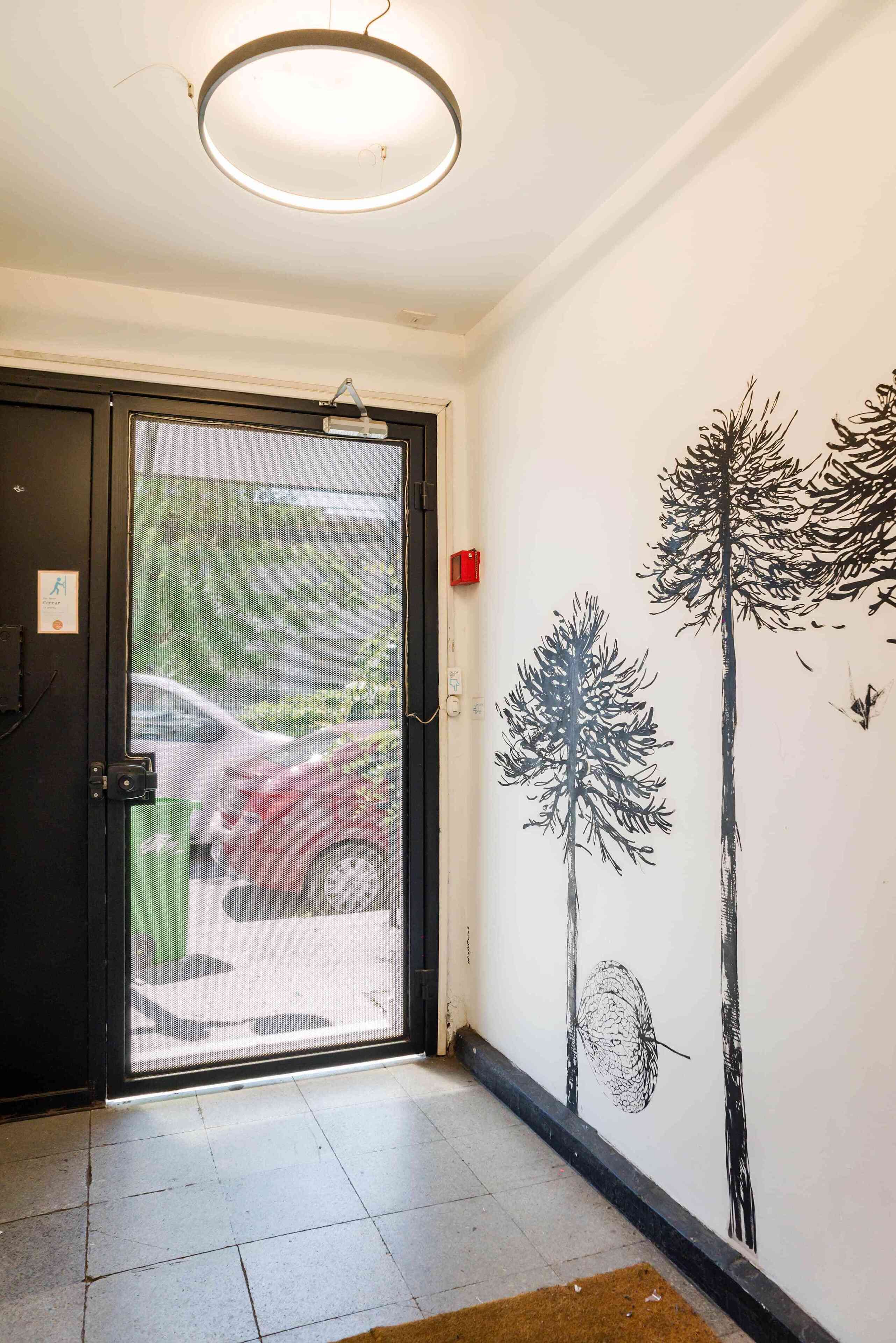 A hotel entrance with a black door, a green trash bin, and a wall mural of trees.